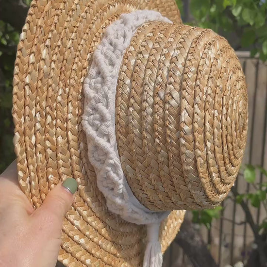 Video showing a wicker hat hanging from the branch of a pear tree, with a handmade boho style macrame hat band wrapped around the crown of the hat, with a long tassel. 