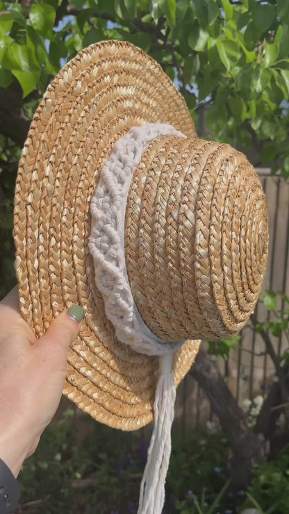 Video showing a wicker hat hanging from the branch of a pear tree, with a handmade boho style macrame hat band wrapped around the crown of the hat, with a long tassel. 
