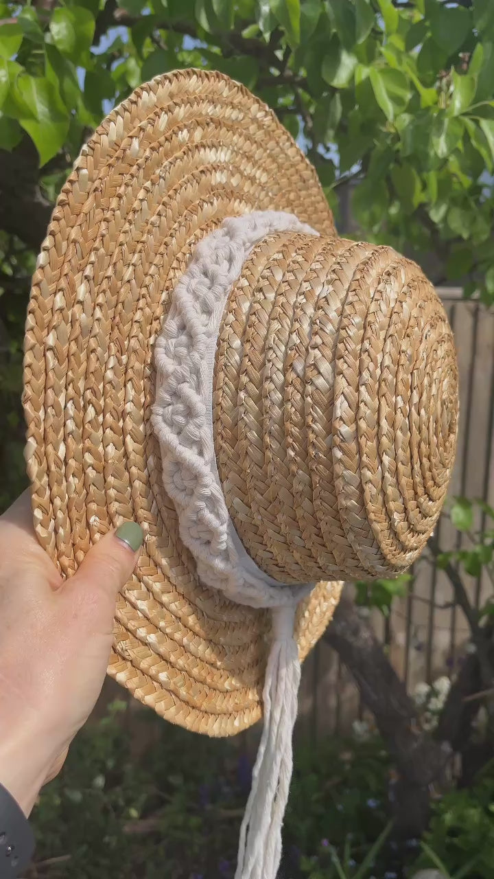 Video showing a wicker hat hanging from the branch of a pear tree, with a handmade boho style macrame hat band wrapped around the crown of the hat, with a long tassel. 