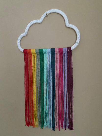 A cloud shaped wall hanging decoration, made with rainbow hanging tassels, displayed against a beige wall.