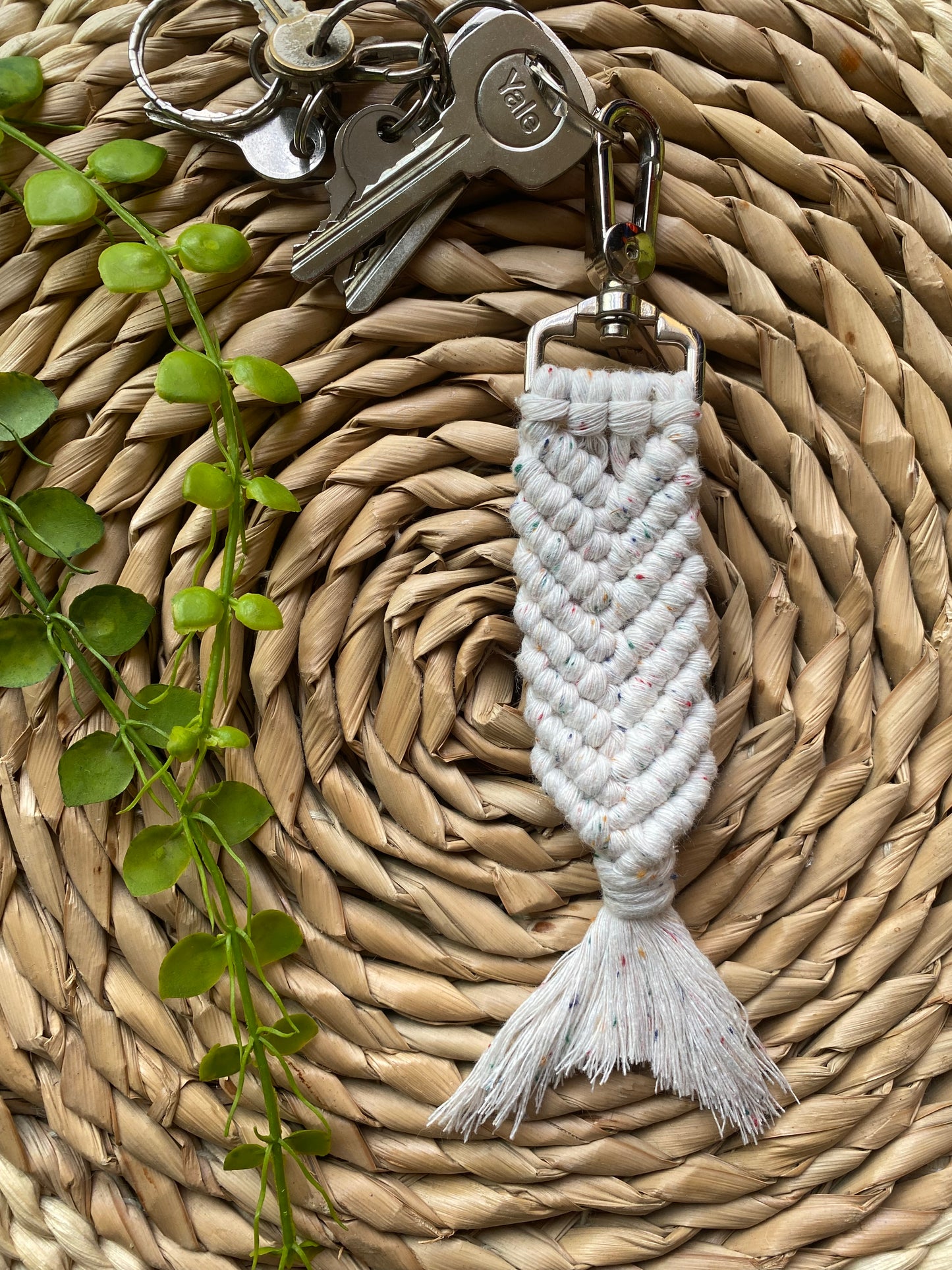 A handmade macrame keyring, knotted using natural coloured recycled cotton, with rainbow flecks, in the shape of a mermaids tail, and finished with a metal lobster clasp. Attached to a small set of silver keys.