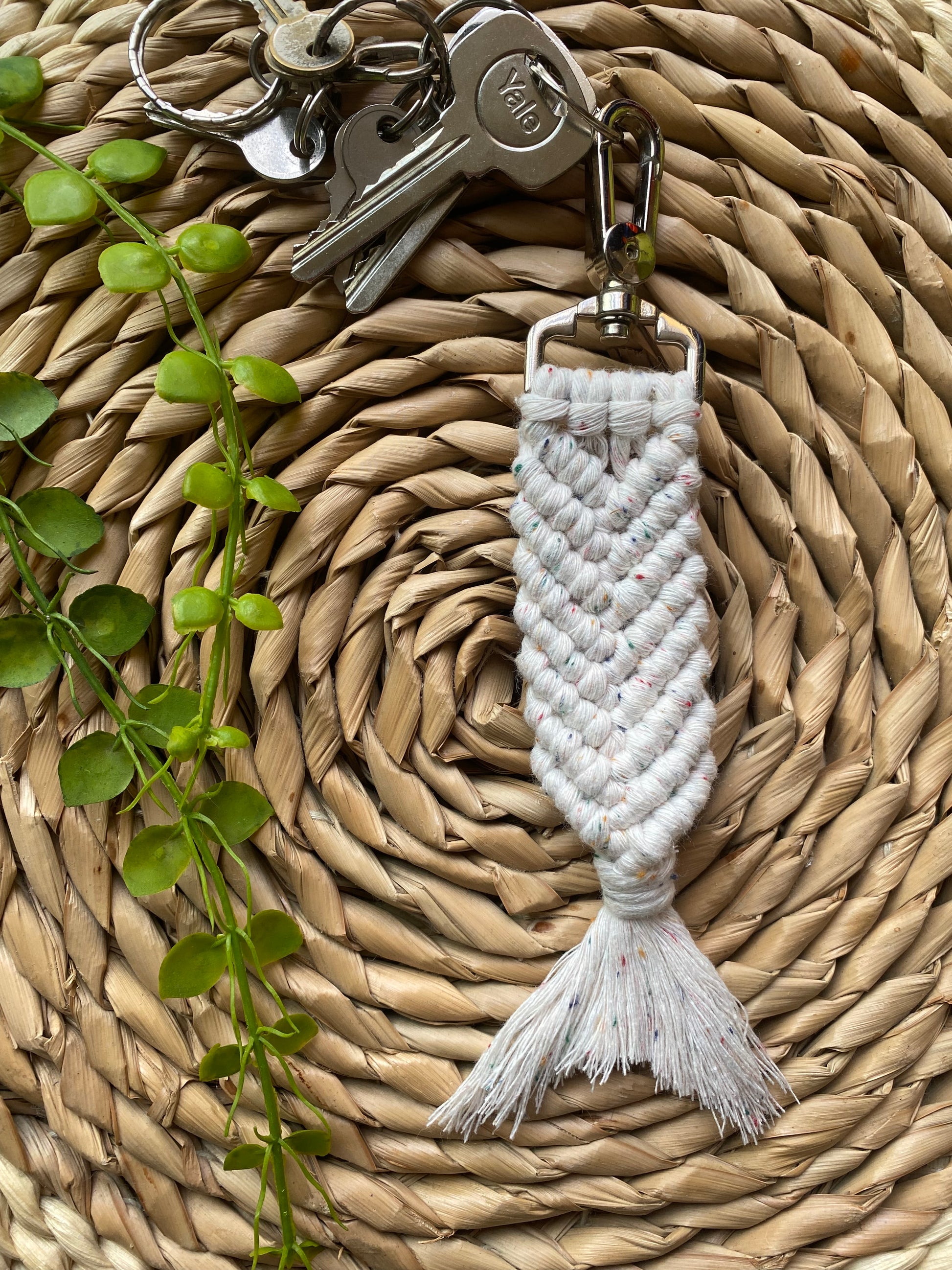 A handmade macrame keyring, knotted using natural coloured recycled cotton, with rainbow flecks, in the shape of a mermaids tail, and finished with a metal lobster clasp. Attached to a small set of silver keys.
