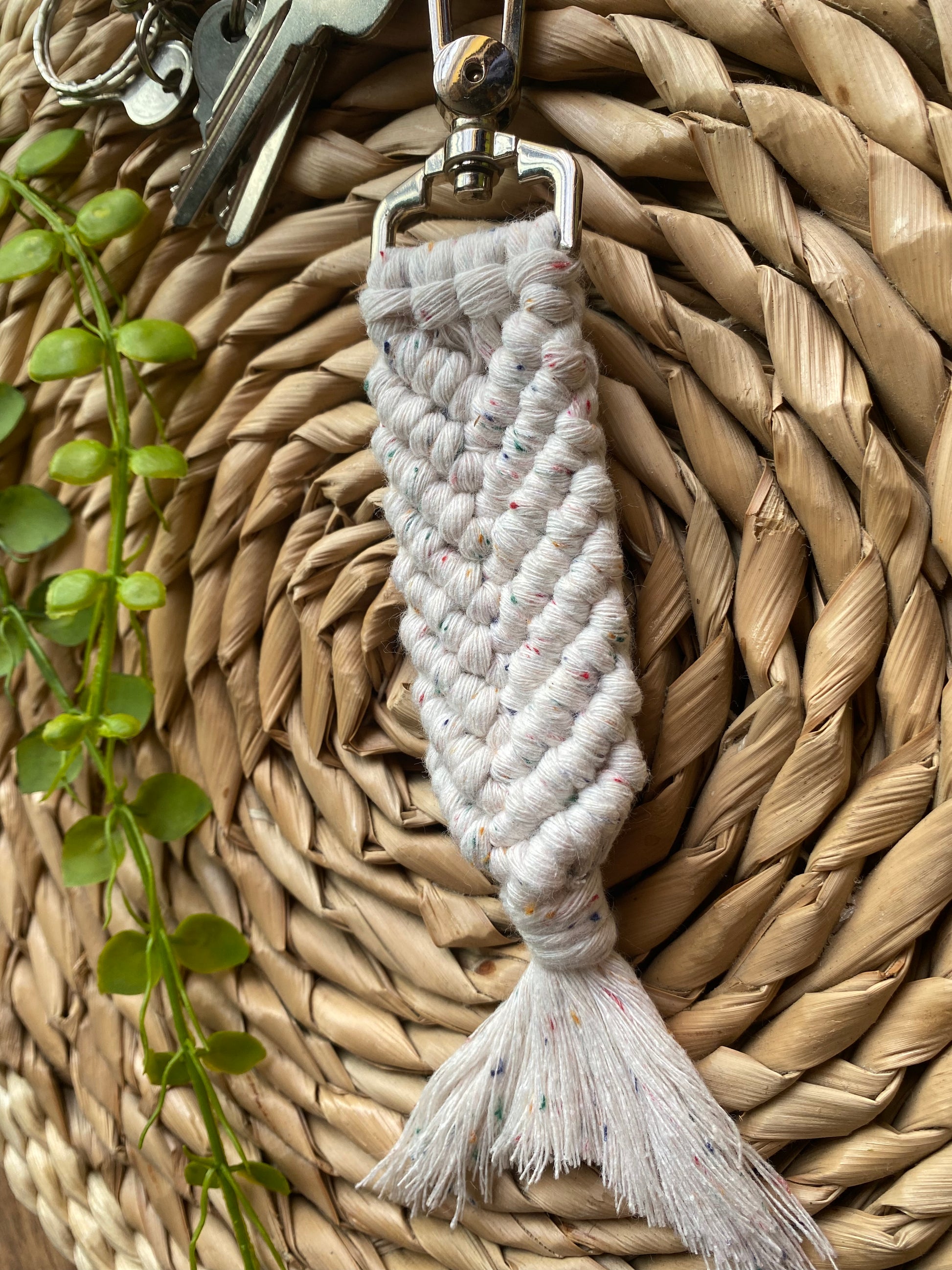 A handmade macrame keyring, knotted using natural coloured recycled cotton, with rainbow flecks, in the shape of a mermaids tail, and finished with a metal lobster clasp. Attached to a small set of silver keys.
