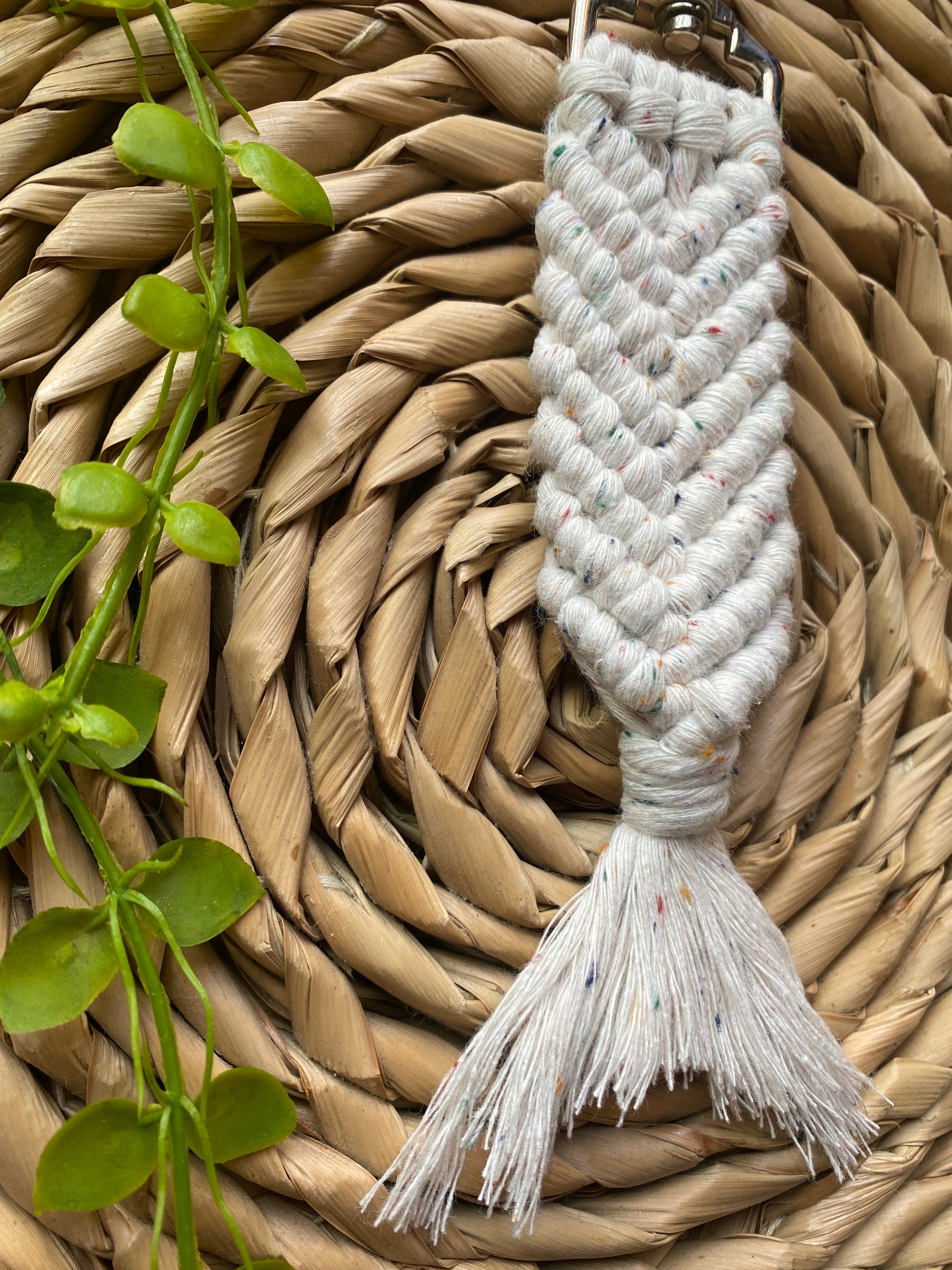 A handmade macrame keyring, knotted using natural coloured recycled cotton, with rainbow flecks, in the shape of a mermaids tail, and finished with a metal lobster clasp. 