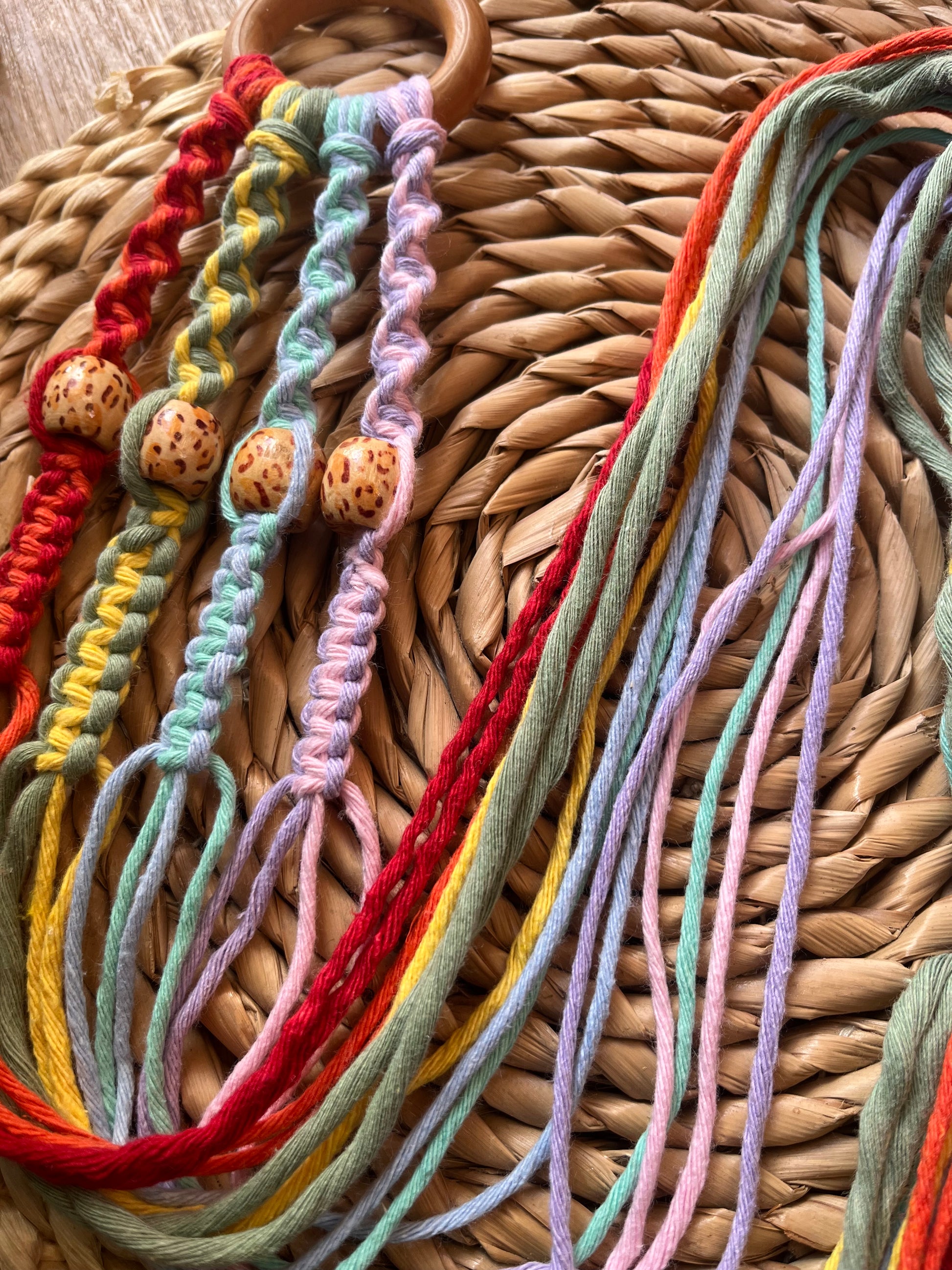 A close up of a multicolored macramé plant hanger with wooden beads coiled on a woven wicker mat. 