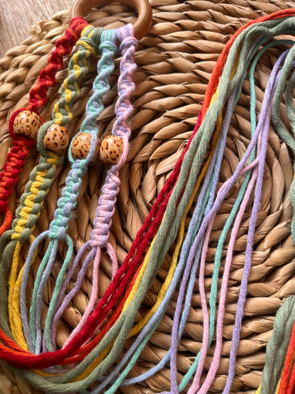A close up of a multicolored macramé plant hanger with wooden beads coiled on a woven wicker mat. 