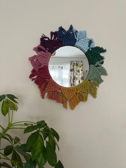 Round wall hanging mirror with rainbow mandala frame, hanging on a beige wall next to a green houseplant.