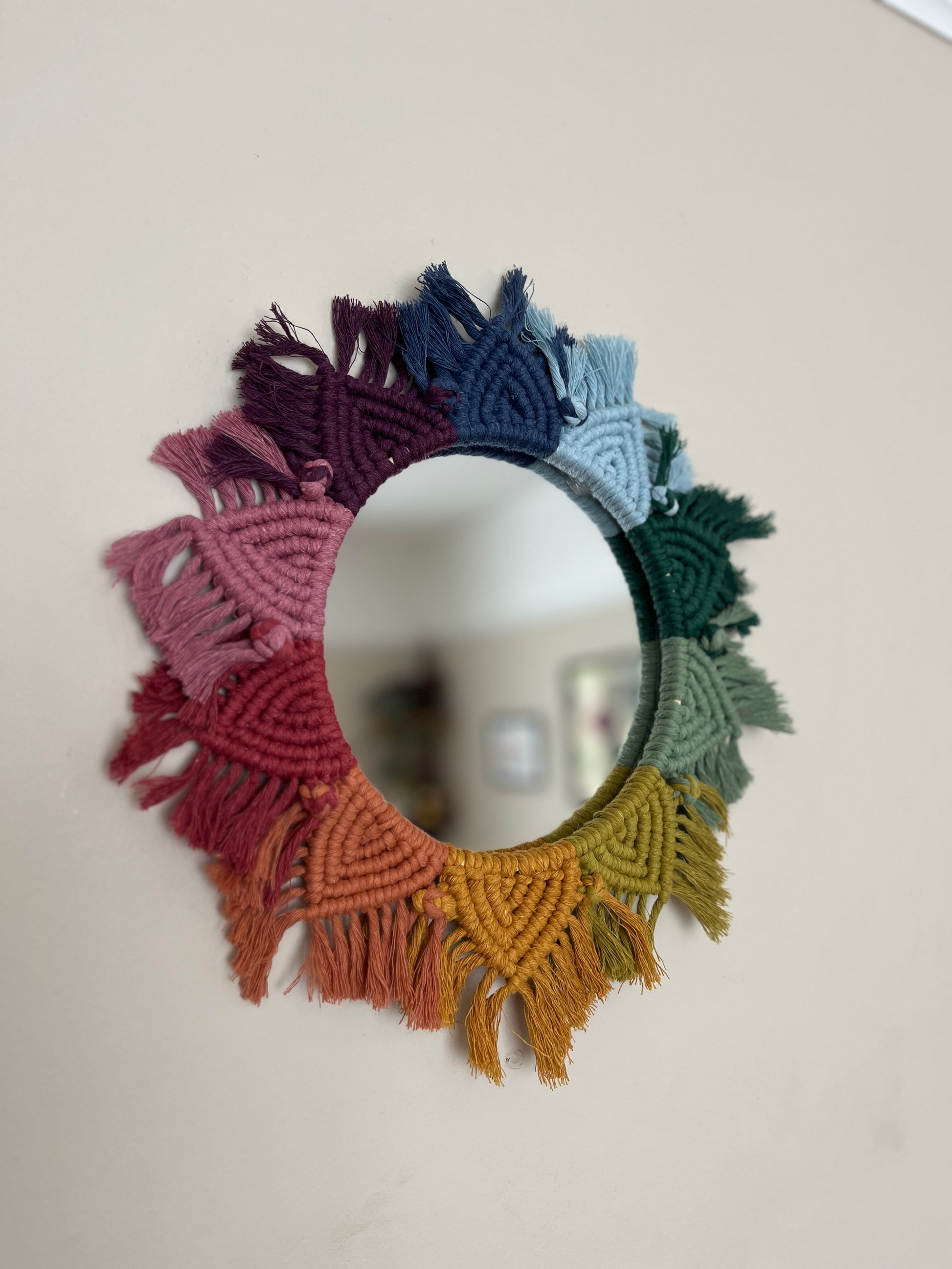 Round wall hanging mirror with rainbow mandala frame, hanging on a beige wall.