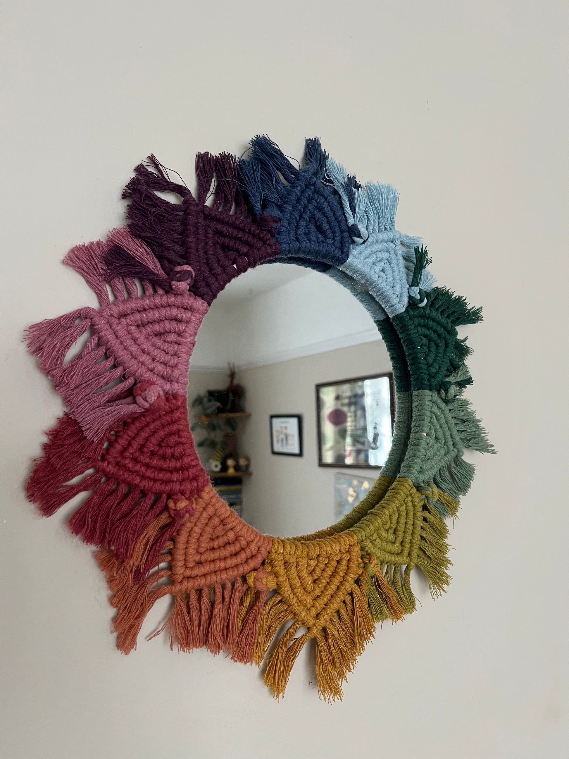 Close up of a round wall hanging mirror with rainbow mandala frame, hanging on a beige wall.