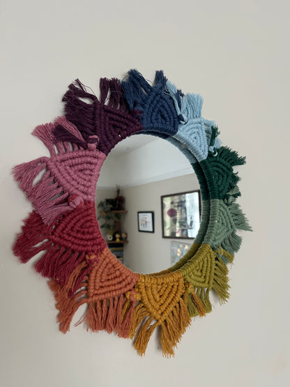 Close up of a round wall hanging mirror with rainbow mandala frame, hanging on a beige wall.