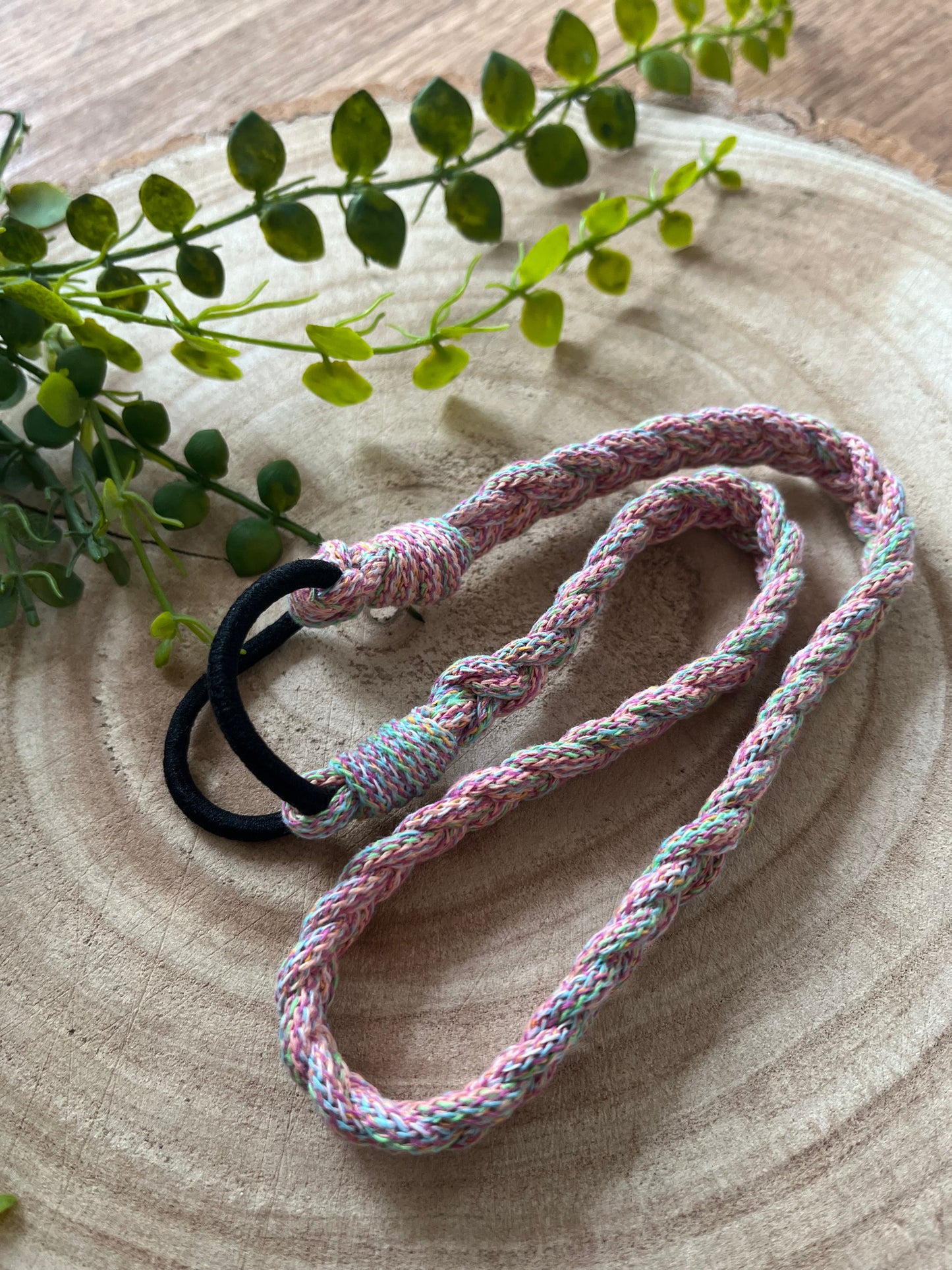 A multicoloured stretchy braided headband folded on a wooden board. 