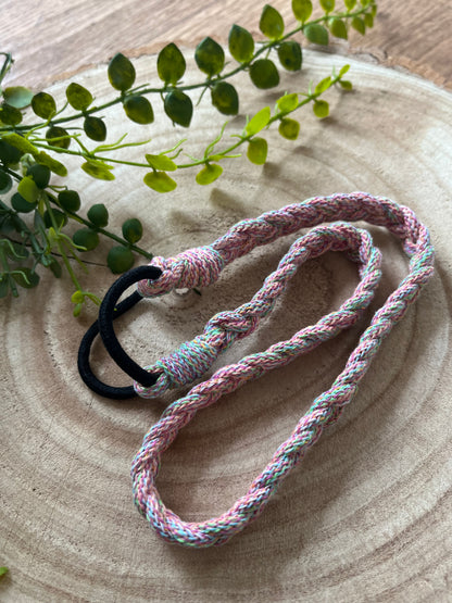 A multicoloured stretchy braided headband folded on a wooden board. 