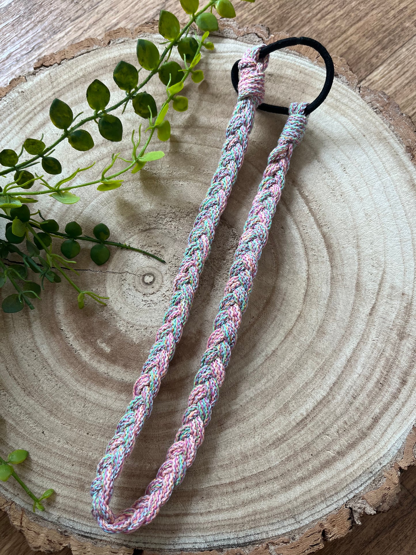 A handmade multicoloured stretchy braided headband on a wooden board.
