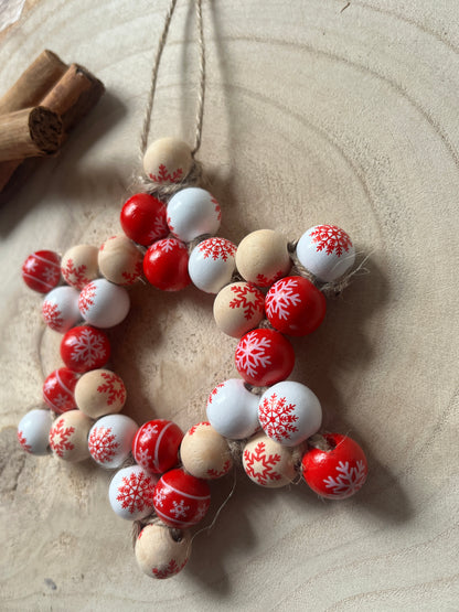 Decorative star shaped wreath made with red, white, and beige wooden beads, on a wooden surface