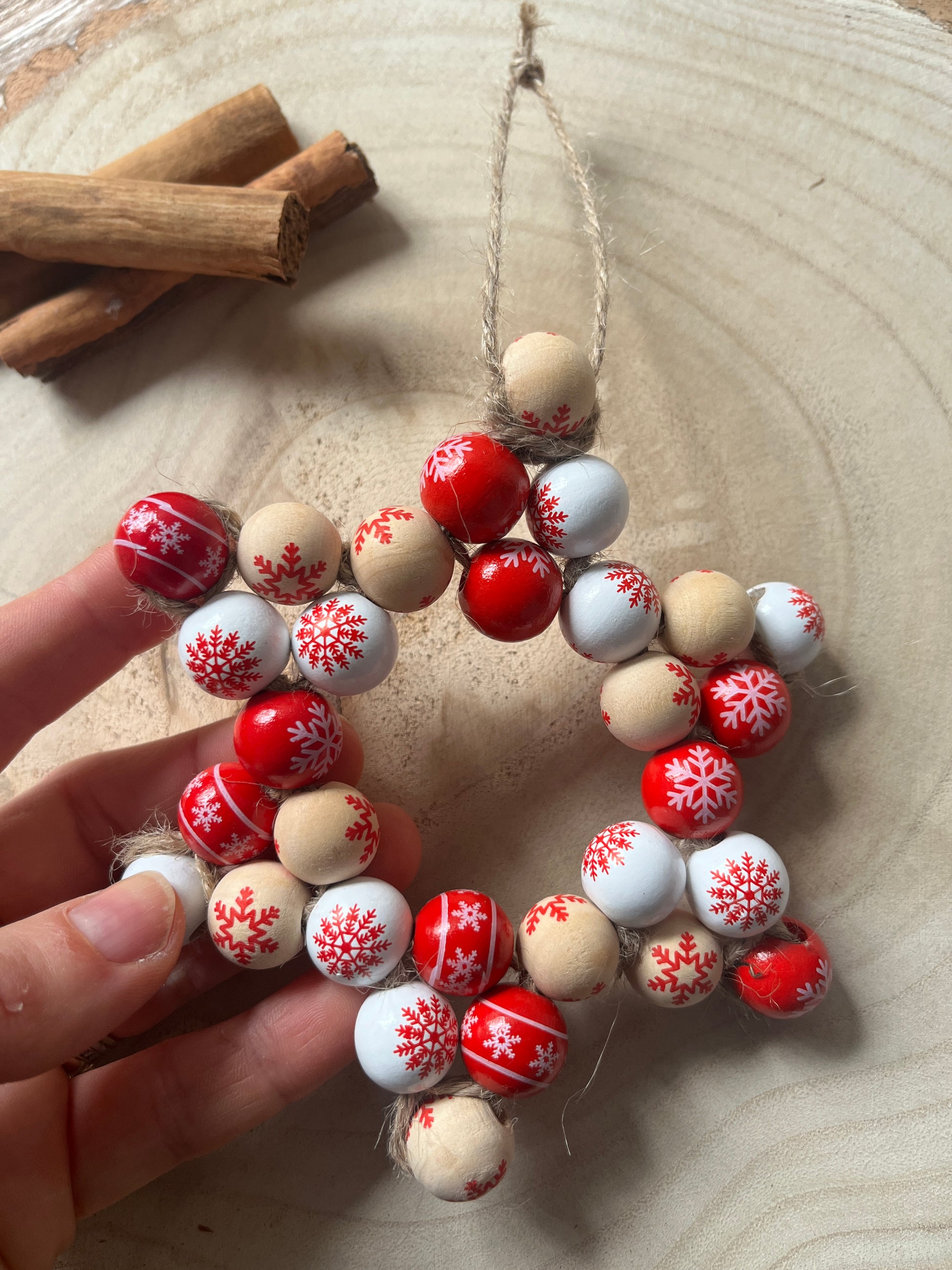 Decorative string of beads with red, white, and beige patterns held by a hand on a wooden surface.