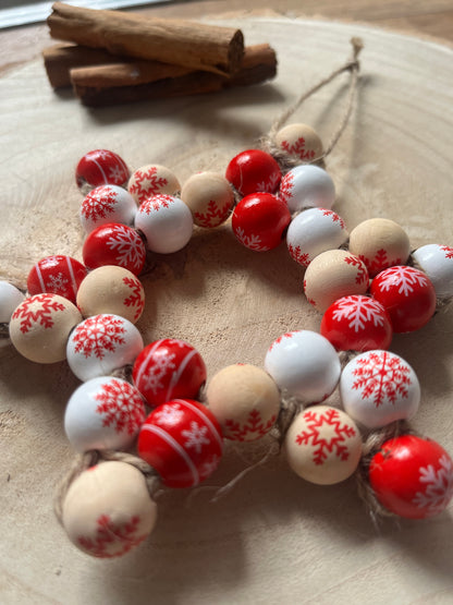 Decorative string of red, white, and beige beads with snowflake patterns on a wooden surface.