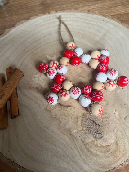 Decorative star made of red, white, and beige beads on a wooden surface.
