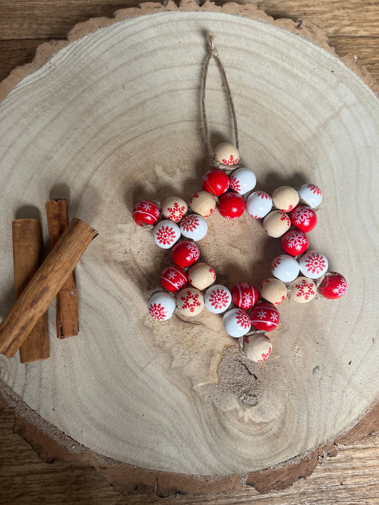 Decorative arrangement of red, white, and beige beads on a wooden surface with cinnamon sticks.