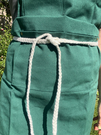 A person stands outside wearing a green apron with a white braided rope waist tie. 