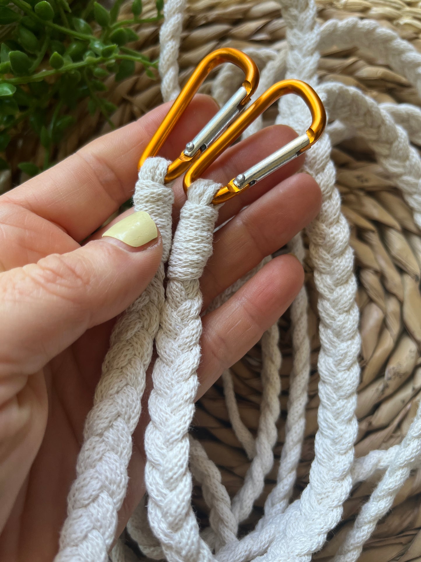 A hand holding orange carabiner clips on the end of a white braided apron strap.