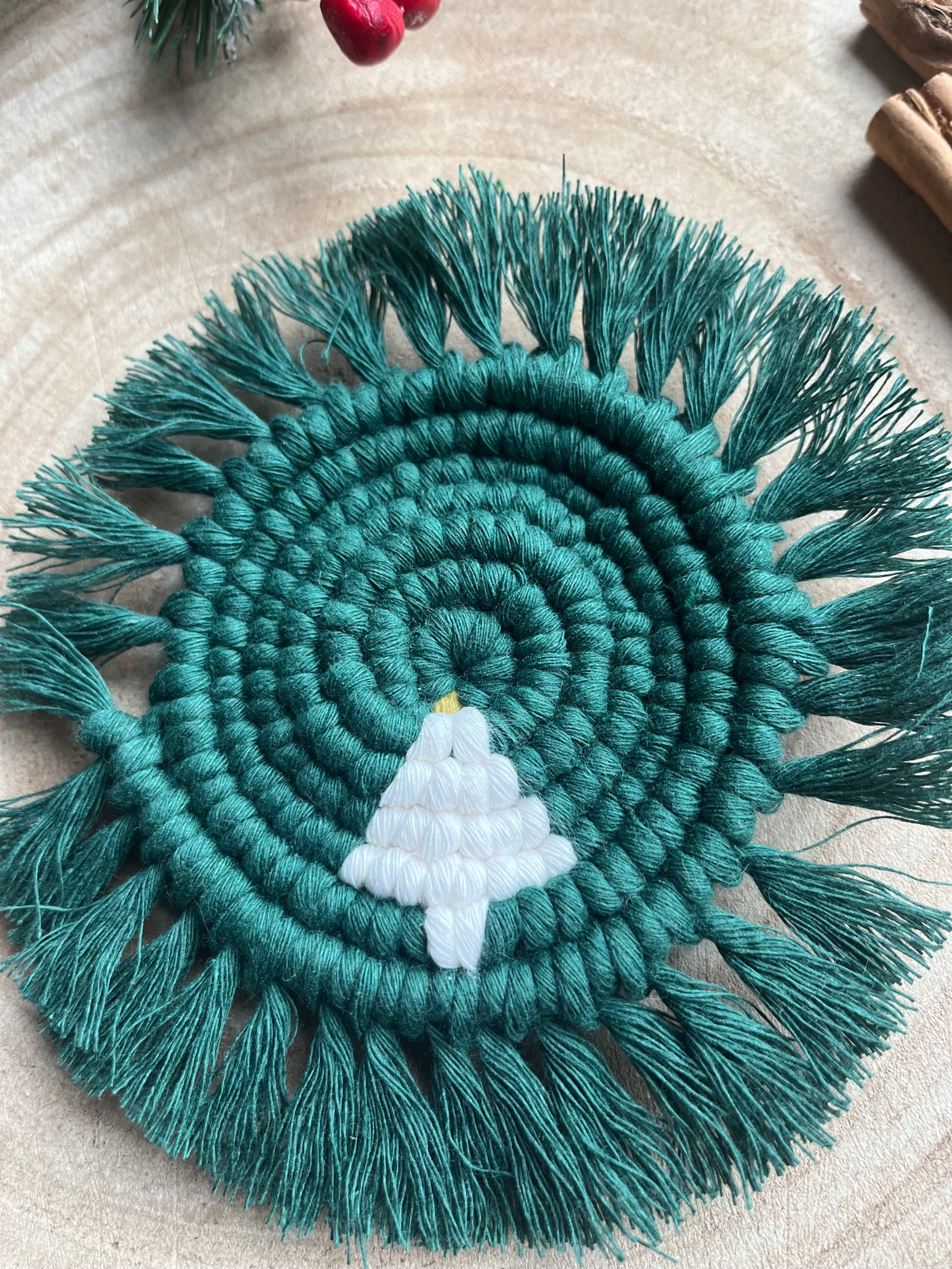 Round macrame coaster with a small christmas tree accent and fringed edge. Handmade with recycled cotton yarn in a pine green colour. 