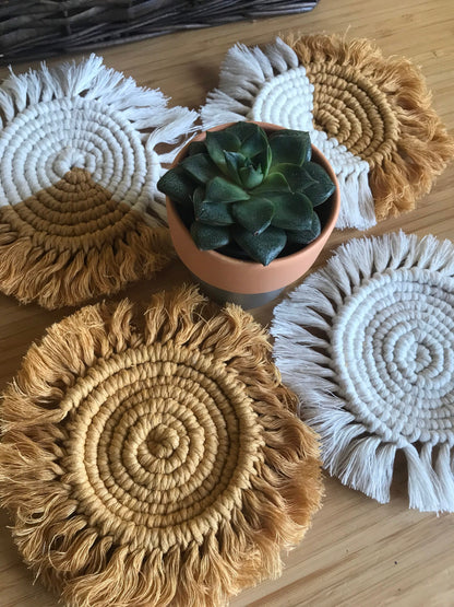 A close up image of a set of 4 round macrame coasters made with mustard yellow and natural yarns, with a soft fringed edge, placed on a wooden table,  with a small succulent houseplant in the middle of them. 