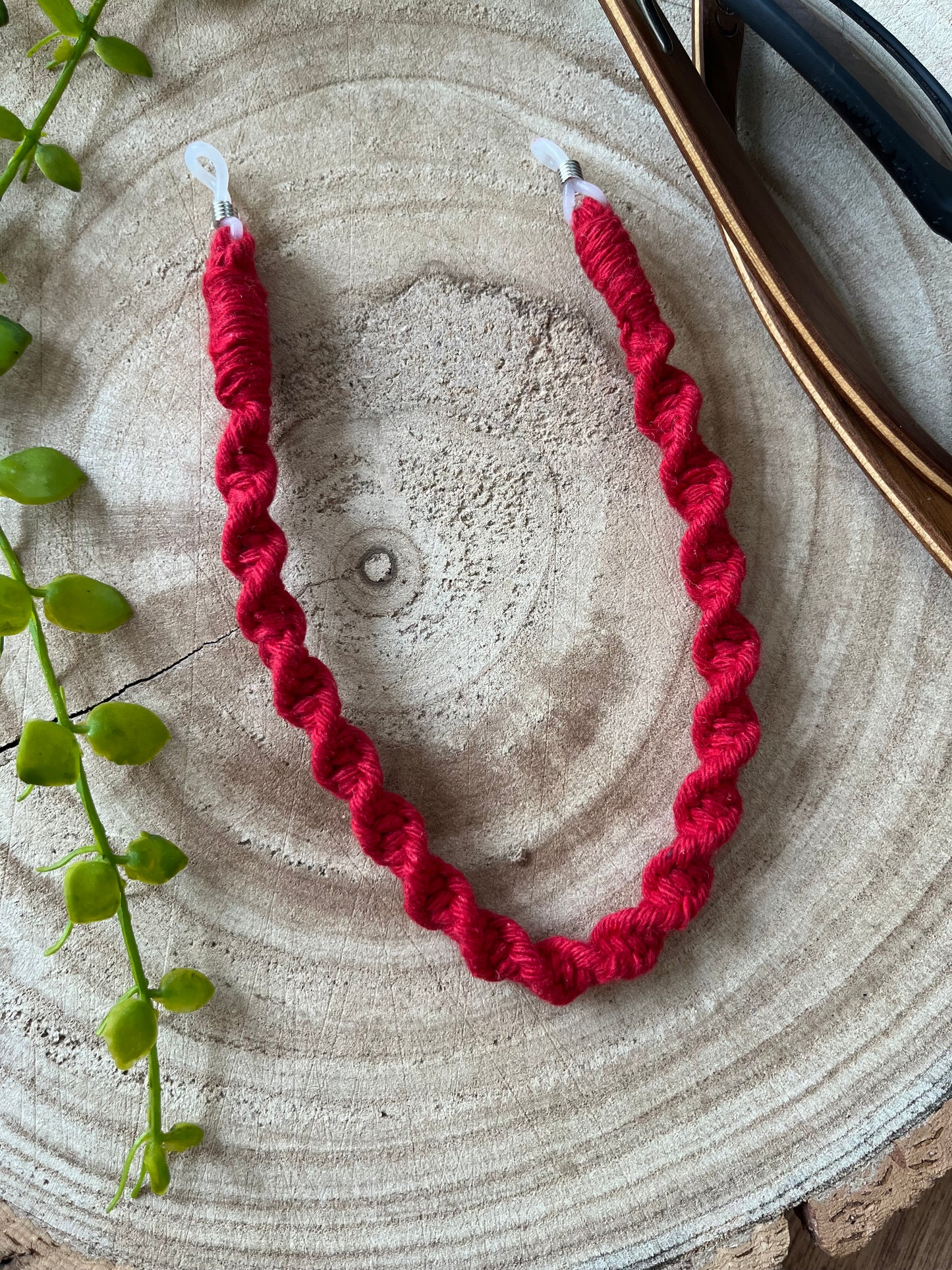 Handmade strap for glasses, made with red recycled cotton, laid on a wooden surface. 