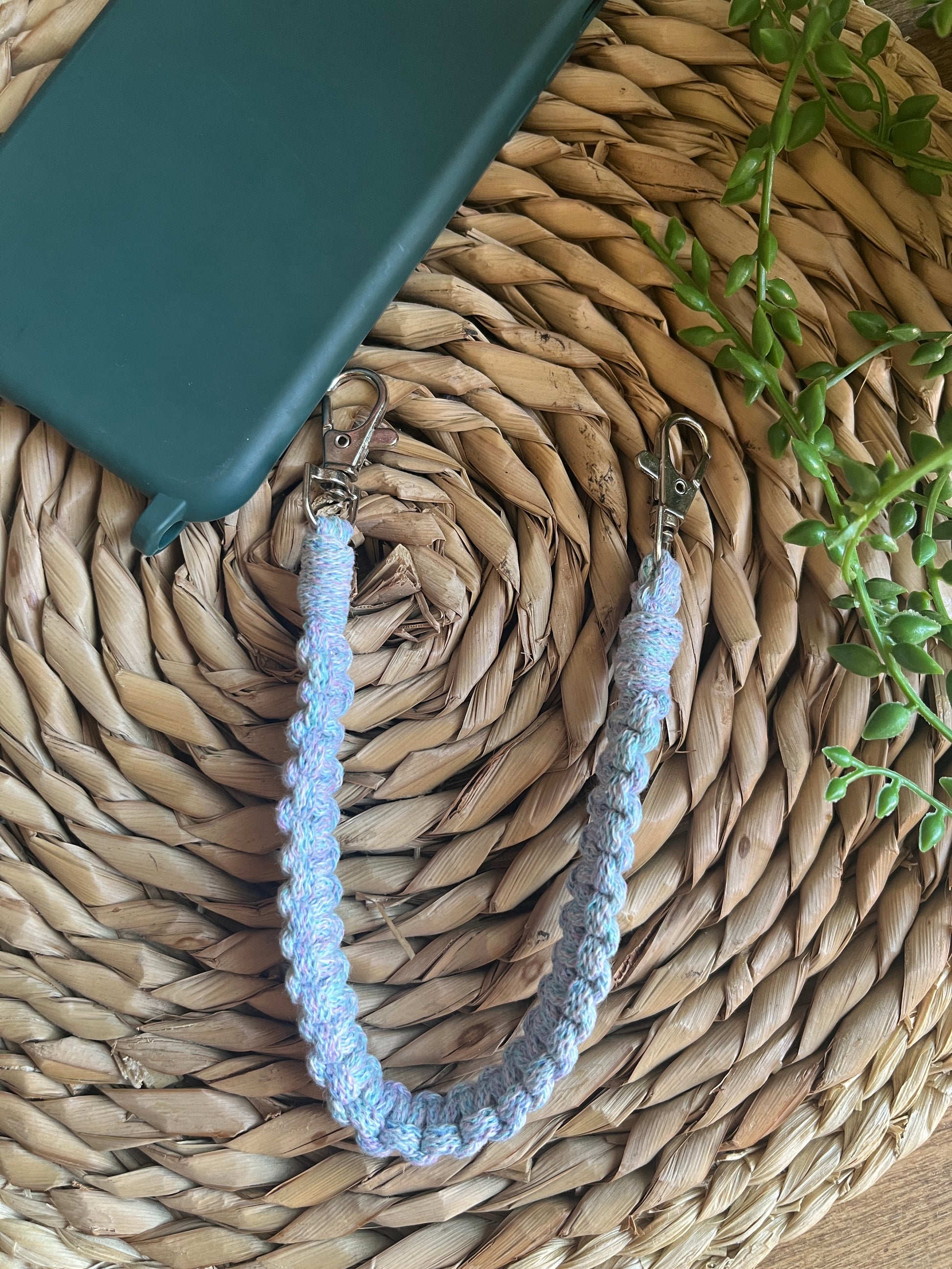 Green phone case on a woven mat, next to a braided blue wristlet with metal clips on each end. 