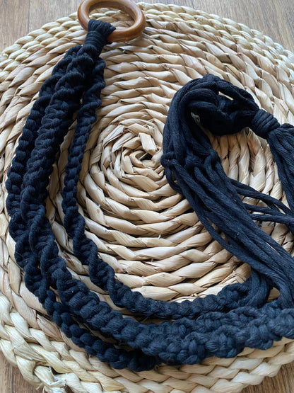Intricately knotted macrame plant hanger, made with black recycled cotton on a wooden hanging ring, coiled on a wicker mat. 