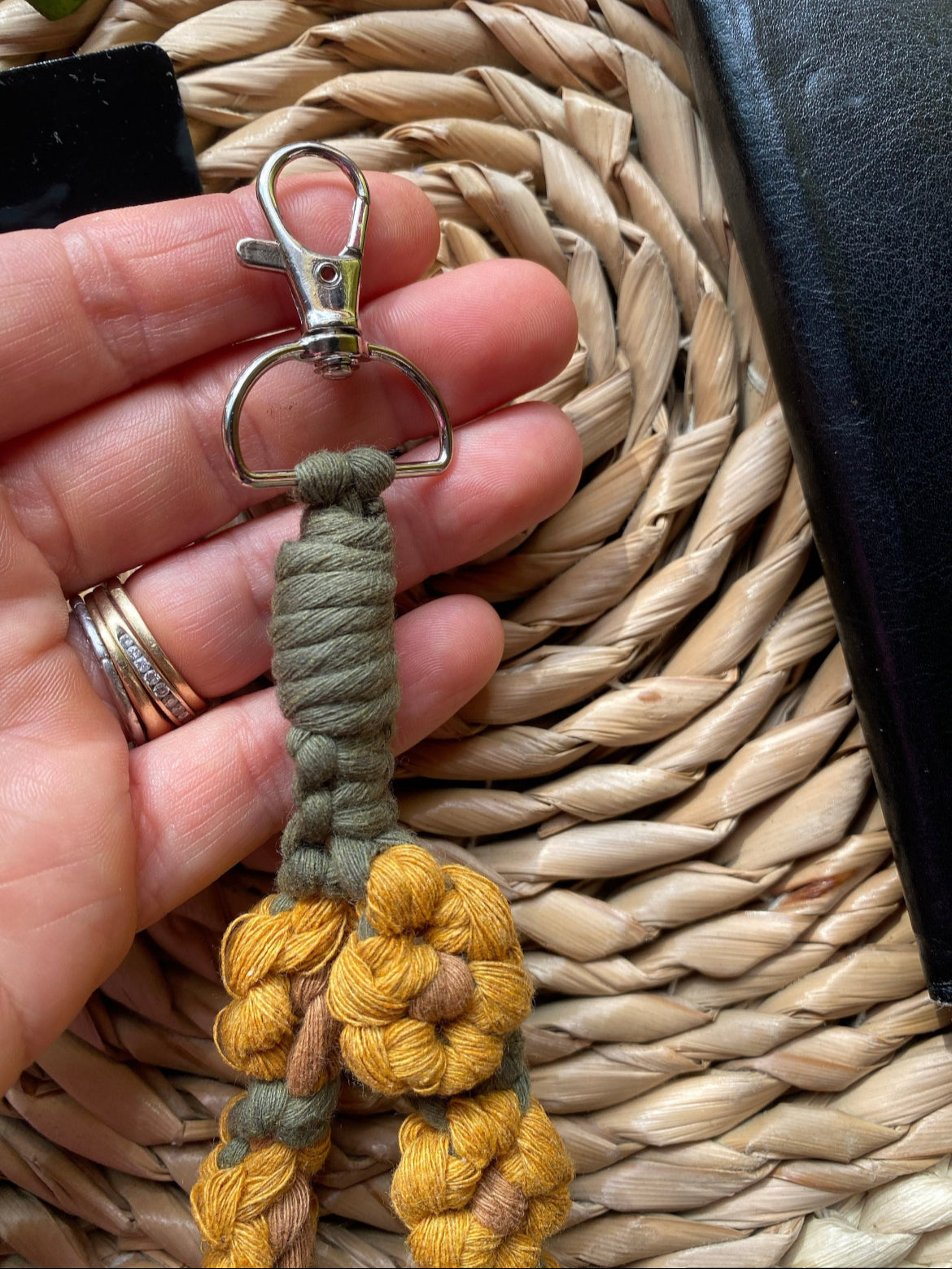 A hand holds the metal clasp on the end of a yellow and green sunflower-themed macramé phone charm wristlet.
