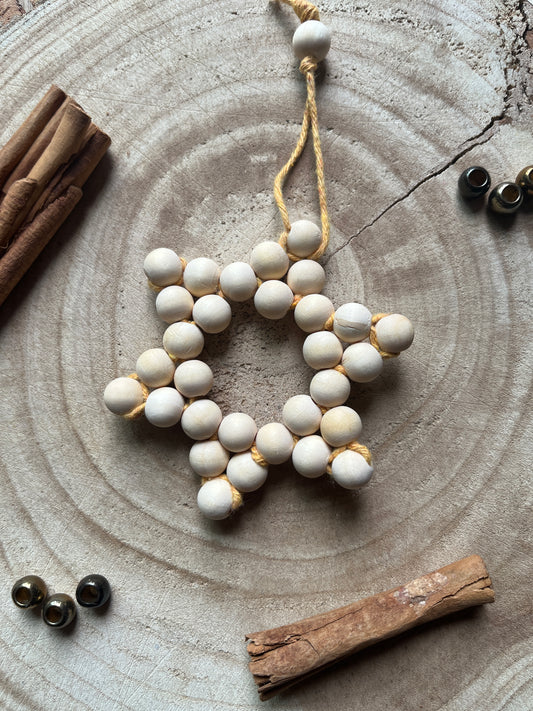 Star-shaped decorative item made of small wooden beads and yellow yarn, on a wooden surface with cinnamon sticks and gold beads for decoration.