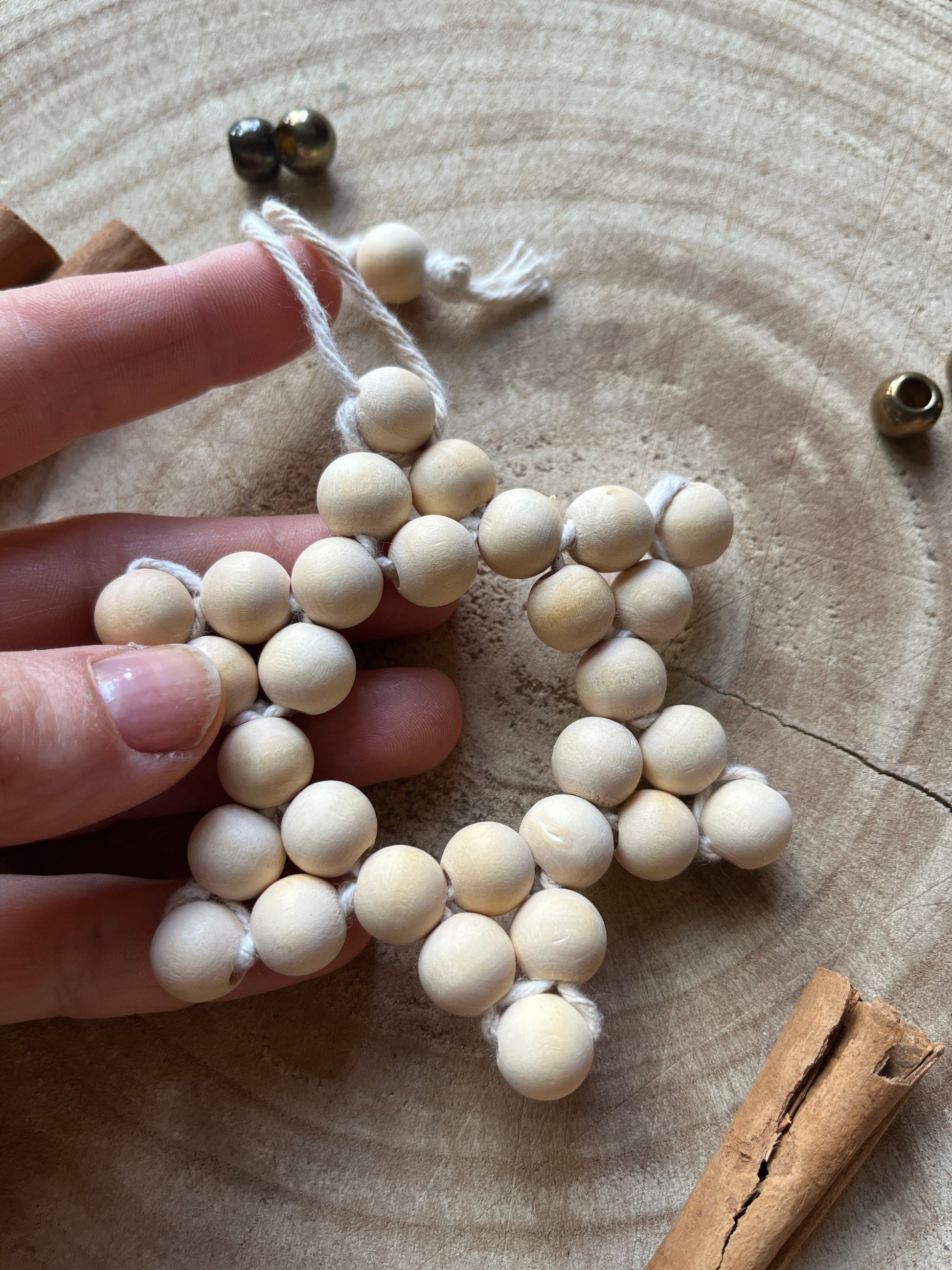 A hand holding a star-shaped hanging decoration, made of small wooden beads and natural yarn.