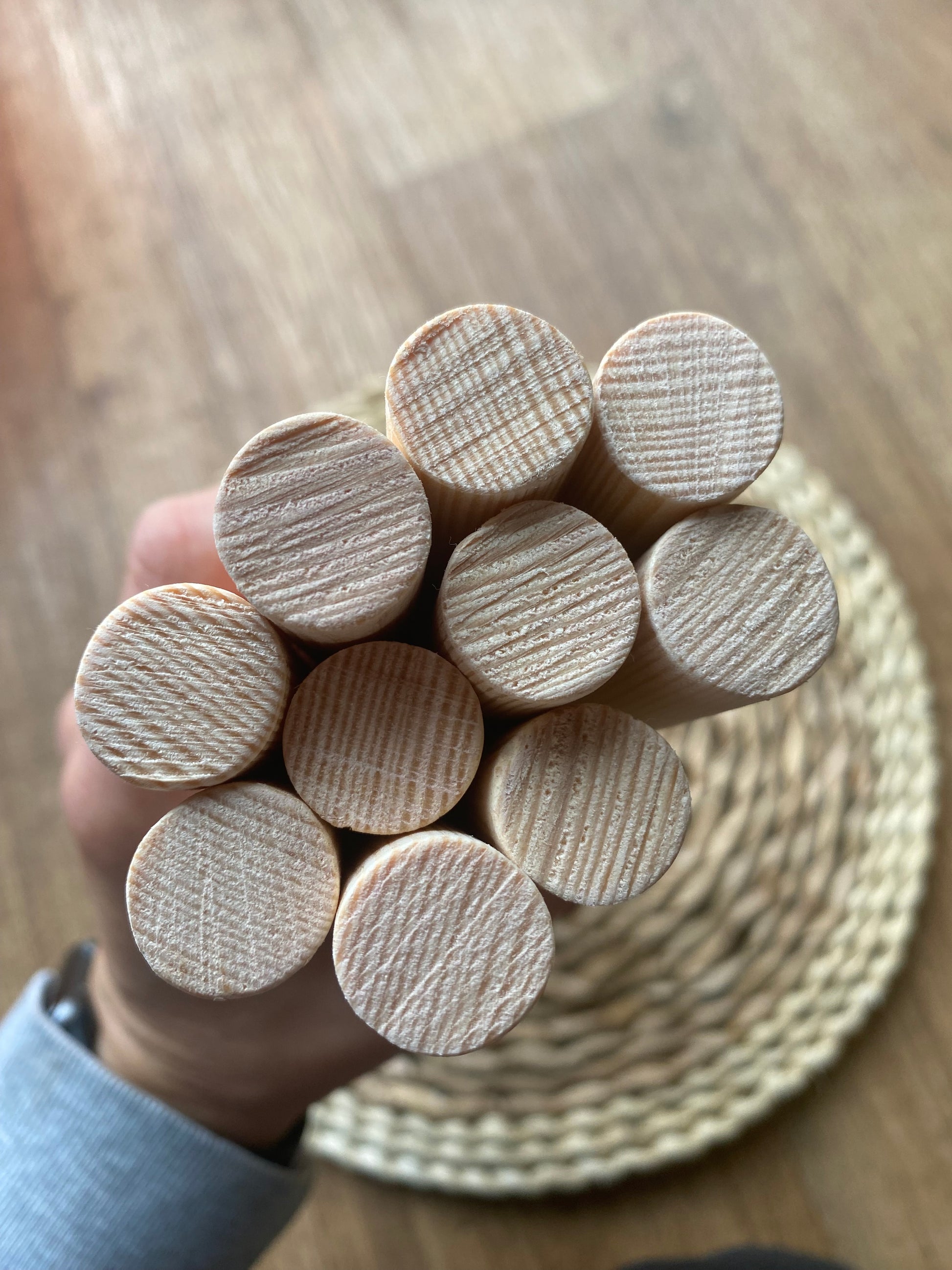 A close up of the natural ends of a pile of natural pine wooden dowels for macramé and crafts held by a person's hand.