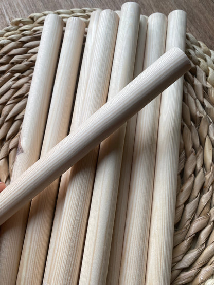 A pile of natural pine wooden dowels for macramé and crafts laid across a round wicker mat. One dowel lays across the others in the opposite direction. 