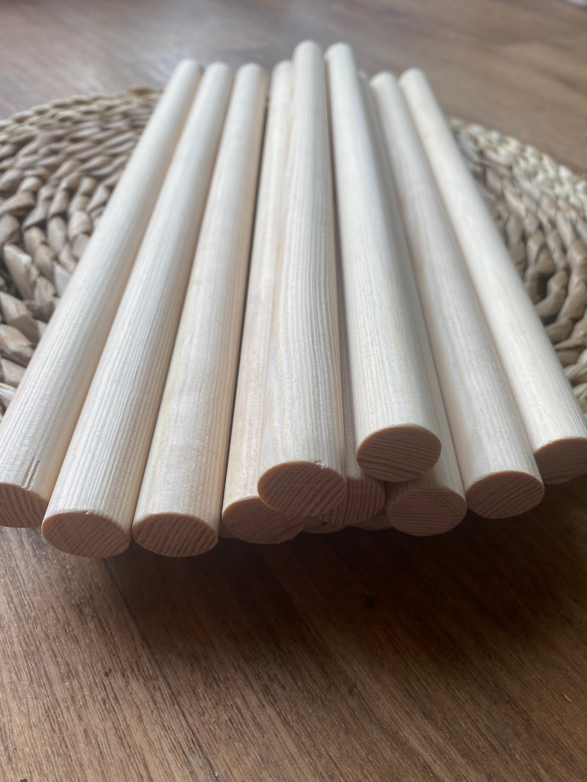 Close up angled view of a pile of natural pine wooden dowels for macramé and crafts laid across a round wicker mat. 