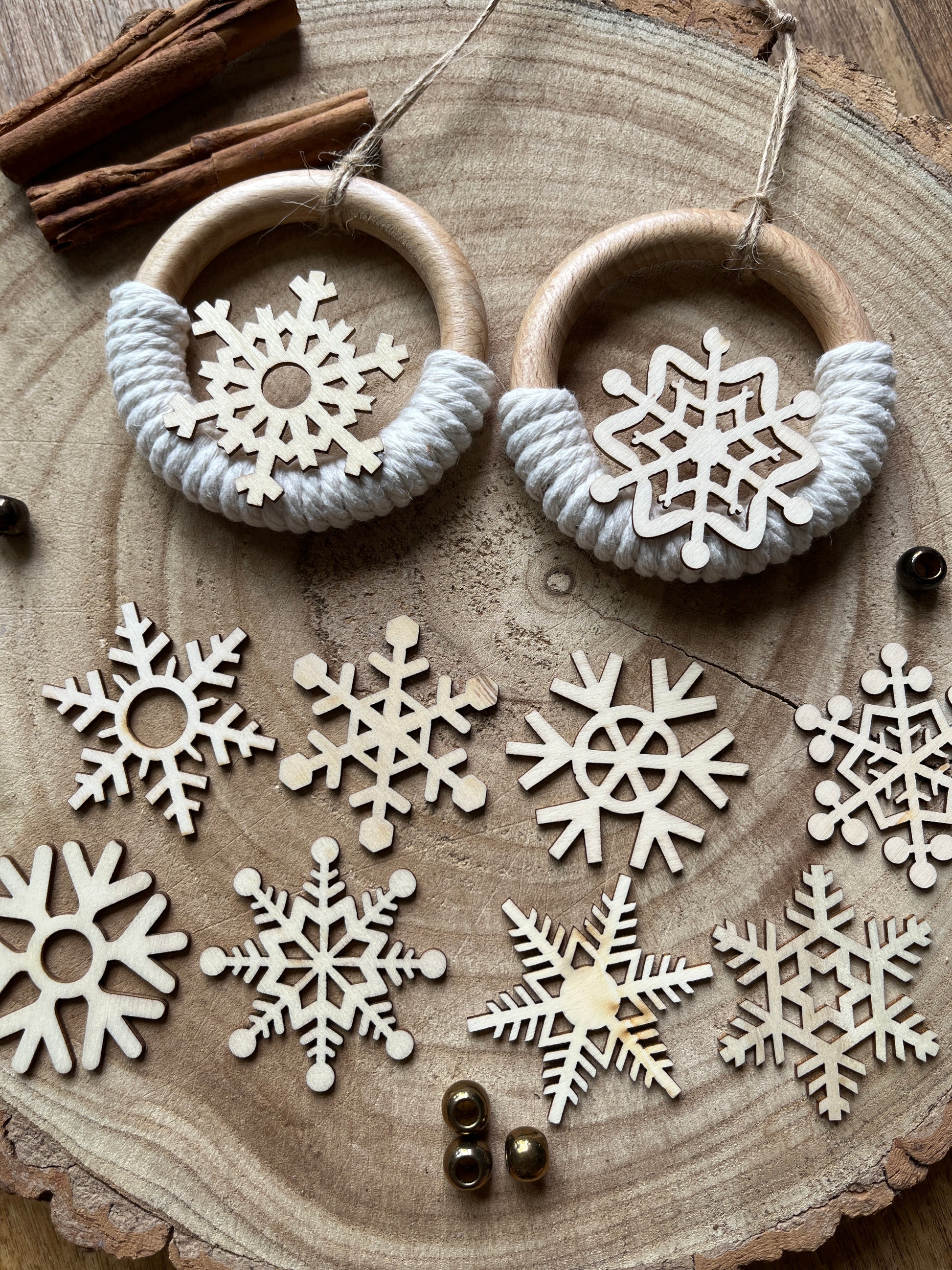 Decorative wooden ornaments, made on wooden rings with natural yarn and finished with wooden snowflake designs, displayed on a rustic wooden surface with lots of different cut out wooden snowflakes underneath. 