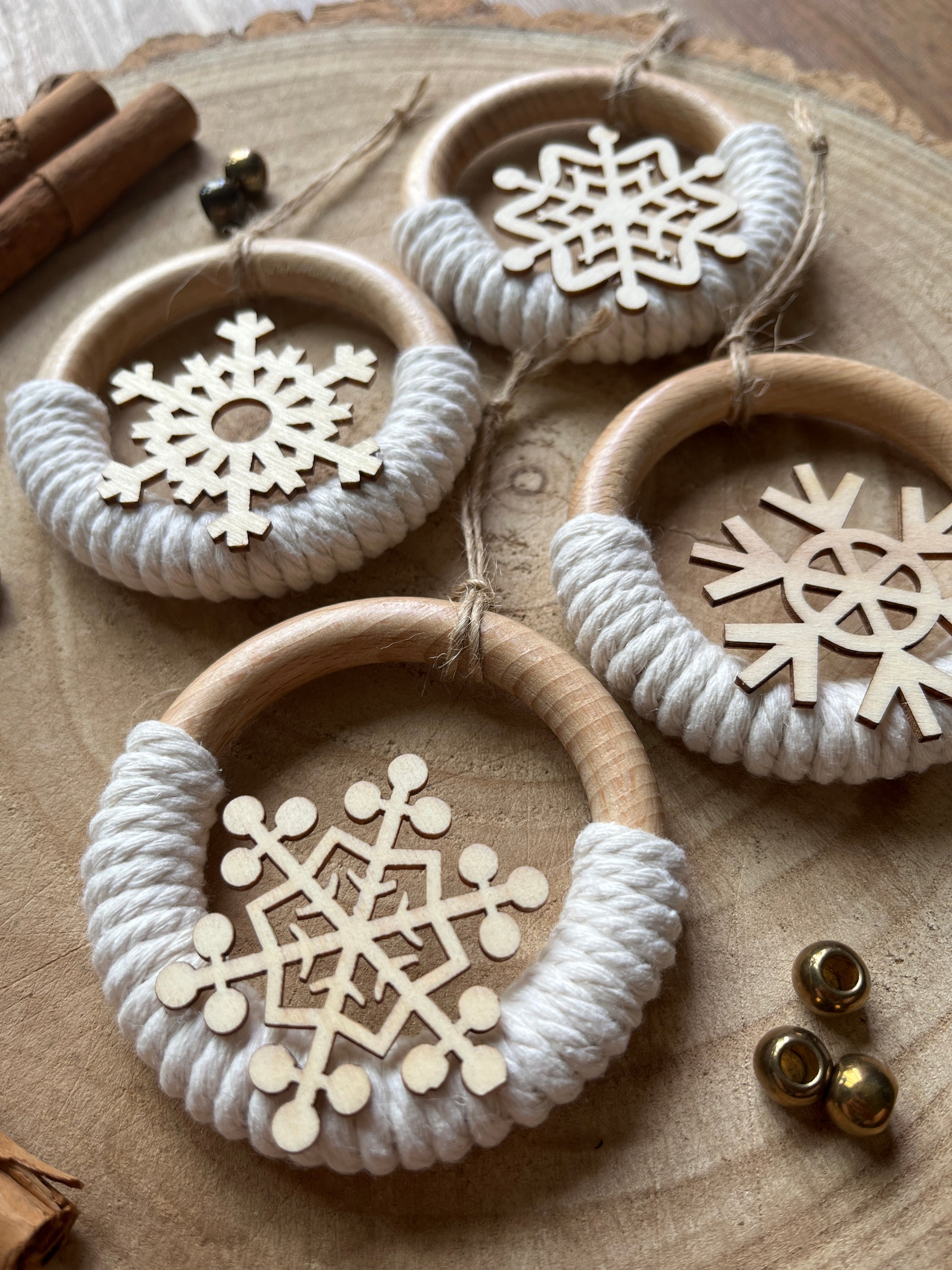 Close up of four decorative wooden ornaments, made on wooden rings with natural yarn and finished with wooden snowflake designs, laid out on a rustic wooden surface.