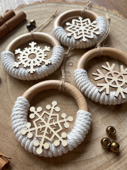 Close up of four decorative wooden ornaments, made on wooden rings with natural yarn and finished with wooden snowflake designs, laid out on a rustic wooden surface.