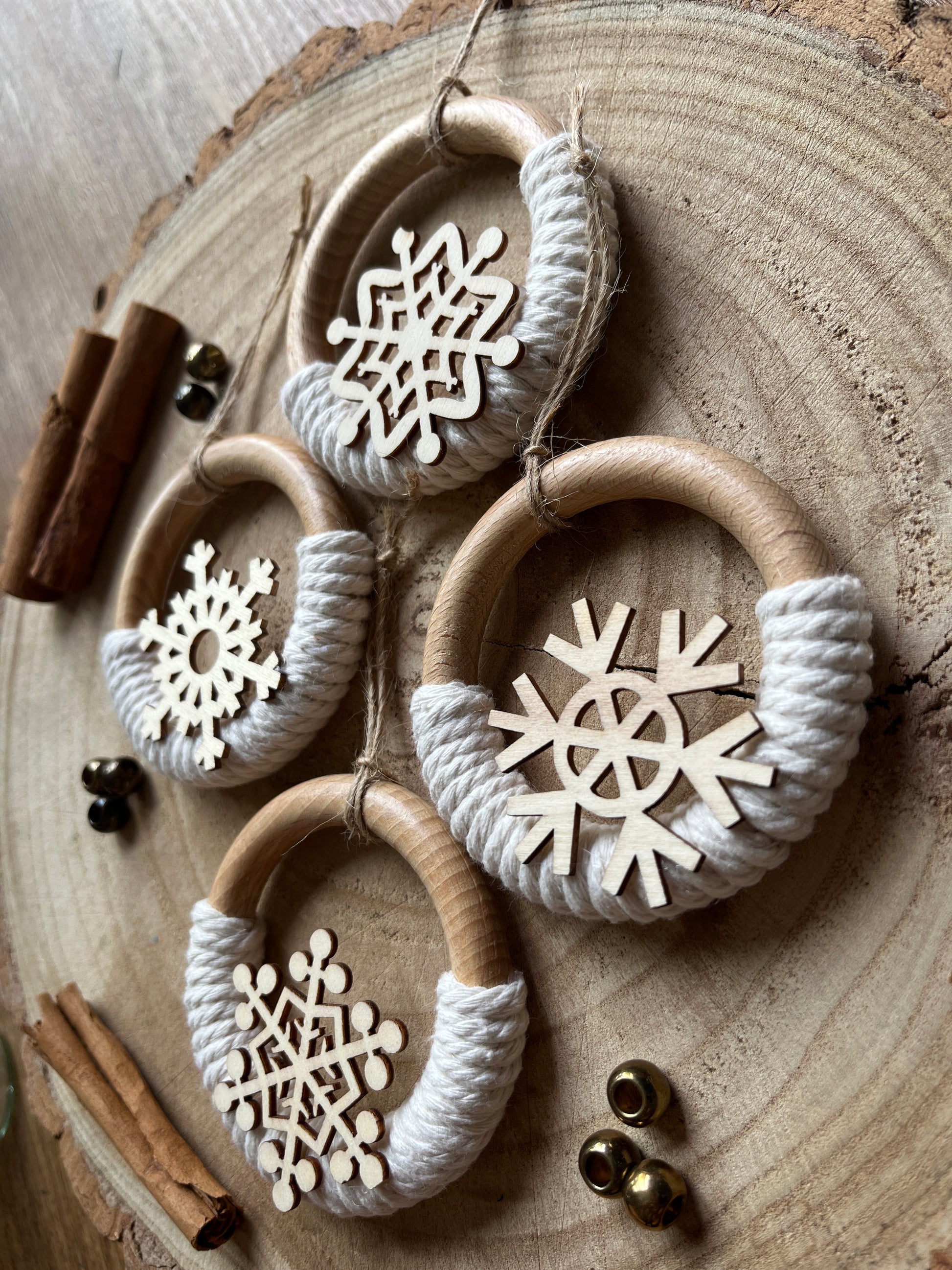 Four decorative wooden ornaments, made on wooden rings with natural yarn and finished with wooden snowflake designs,  on a rustic wooden surface.