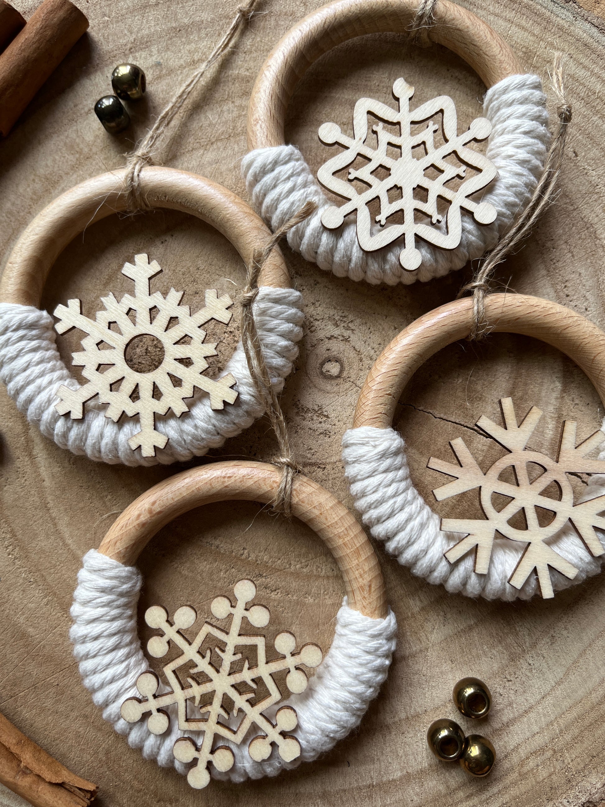 Four decorative wooden hanging ornaments, made on wooden rings with natural yarn and finished with wooden snowflake designs, on a wooden surface.