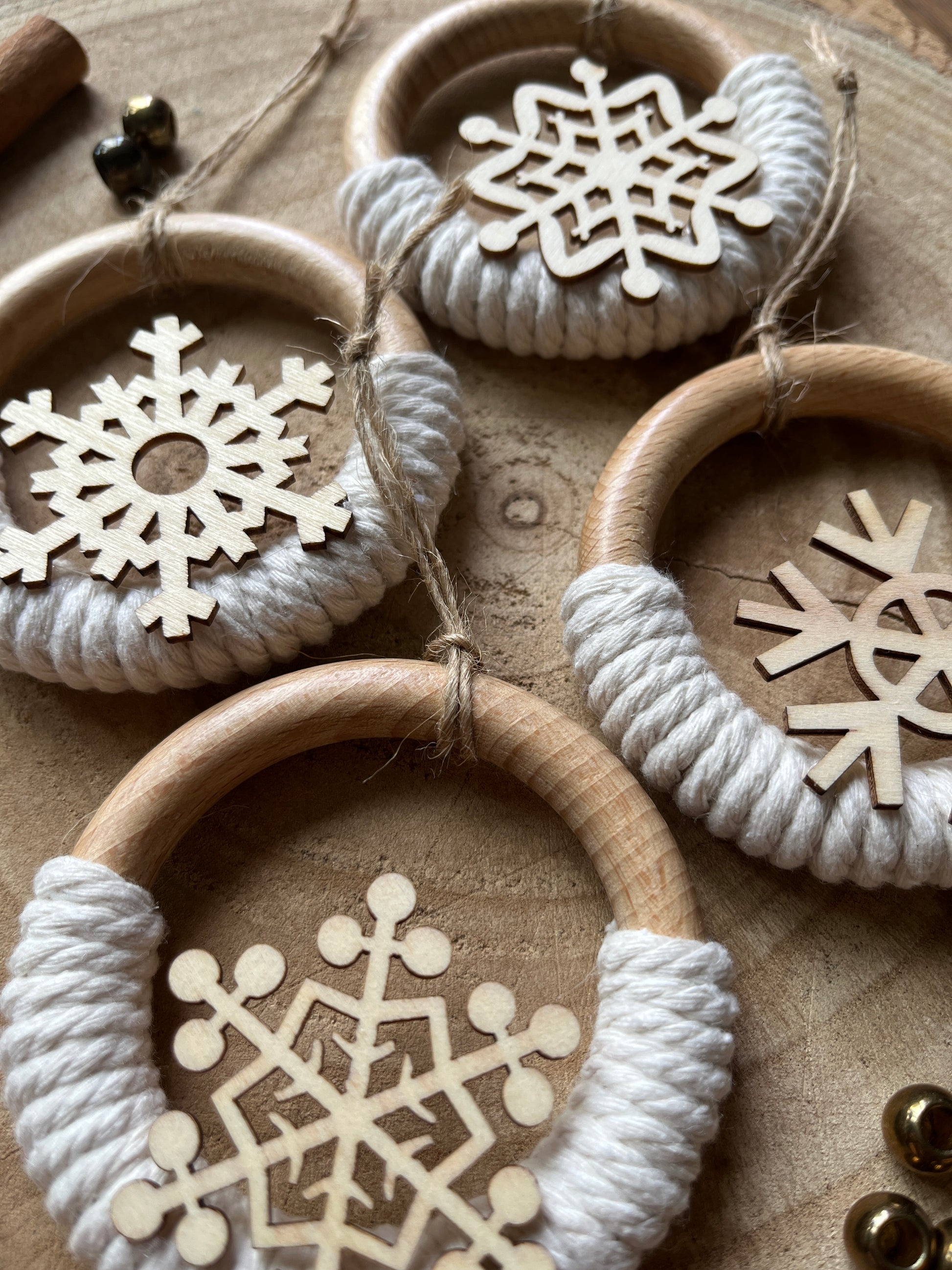 Close up of four decorative wooden ornaments, made on wooden rings with natural yarn and finished with wooden snowflake designs.