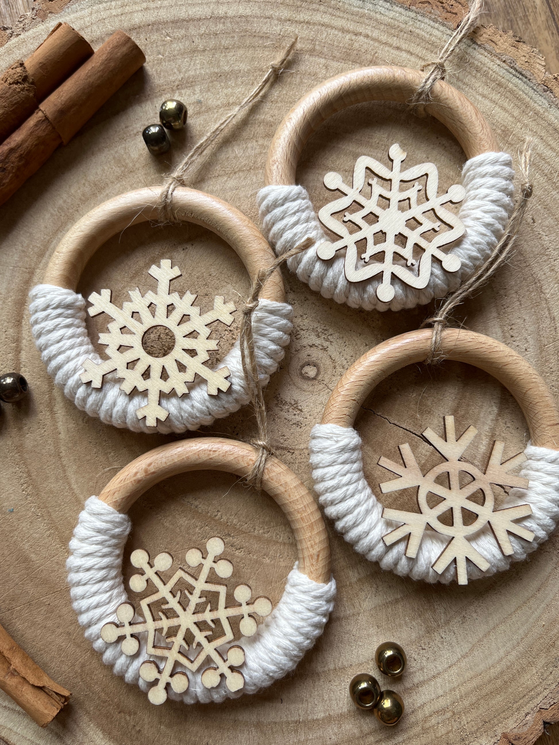 Four decorative wooden ornaments, made on wooden rings with natural yarn and finished with wooden snowflake designs, displayed neatly beside each other on a rustic wooden surface.