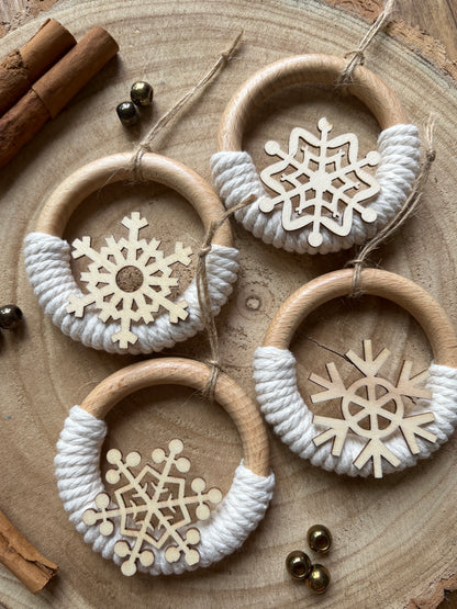 Four decorative wooden ornaments, made on wooden rings with natural yarn and finished with wooden snowflake designs, displayed neatly beside each other on a rustic wooden surface.