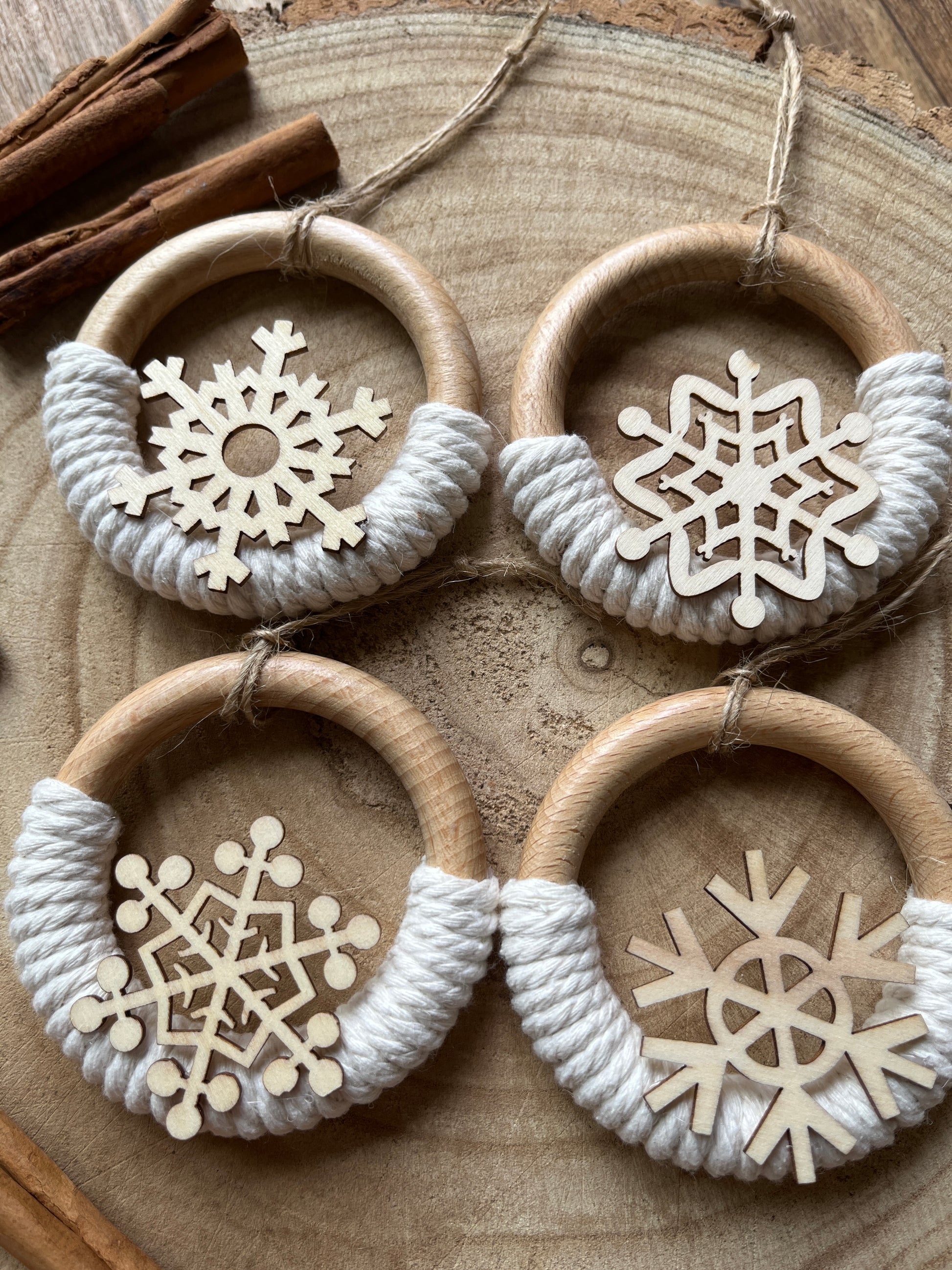 Four decorative wooden ornaments, made on wooden rings with natural yarn and finished with wooden snowflake designs.