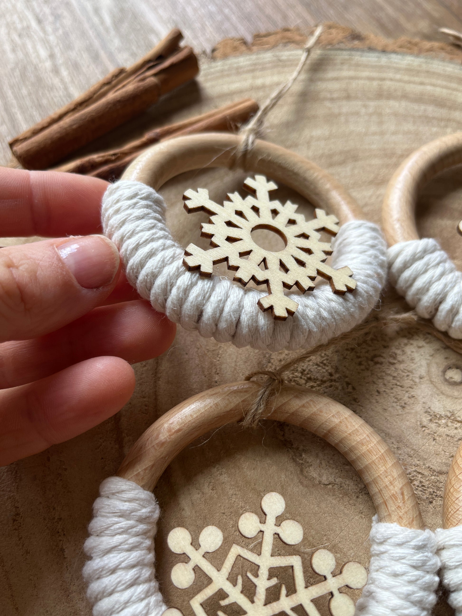 A hand showing a decorative wooden ornament, made on a wooden ring with natural yarn and finished with a cut out wooden snowflake design.