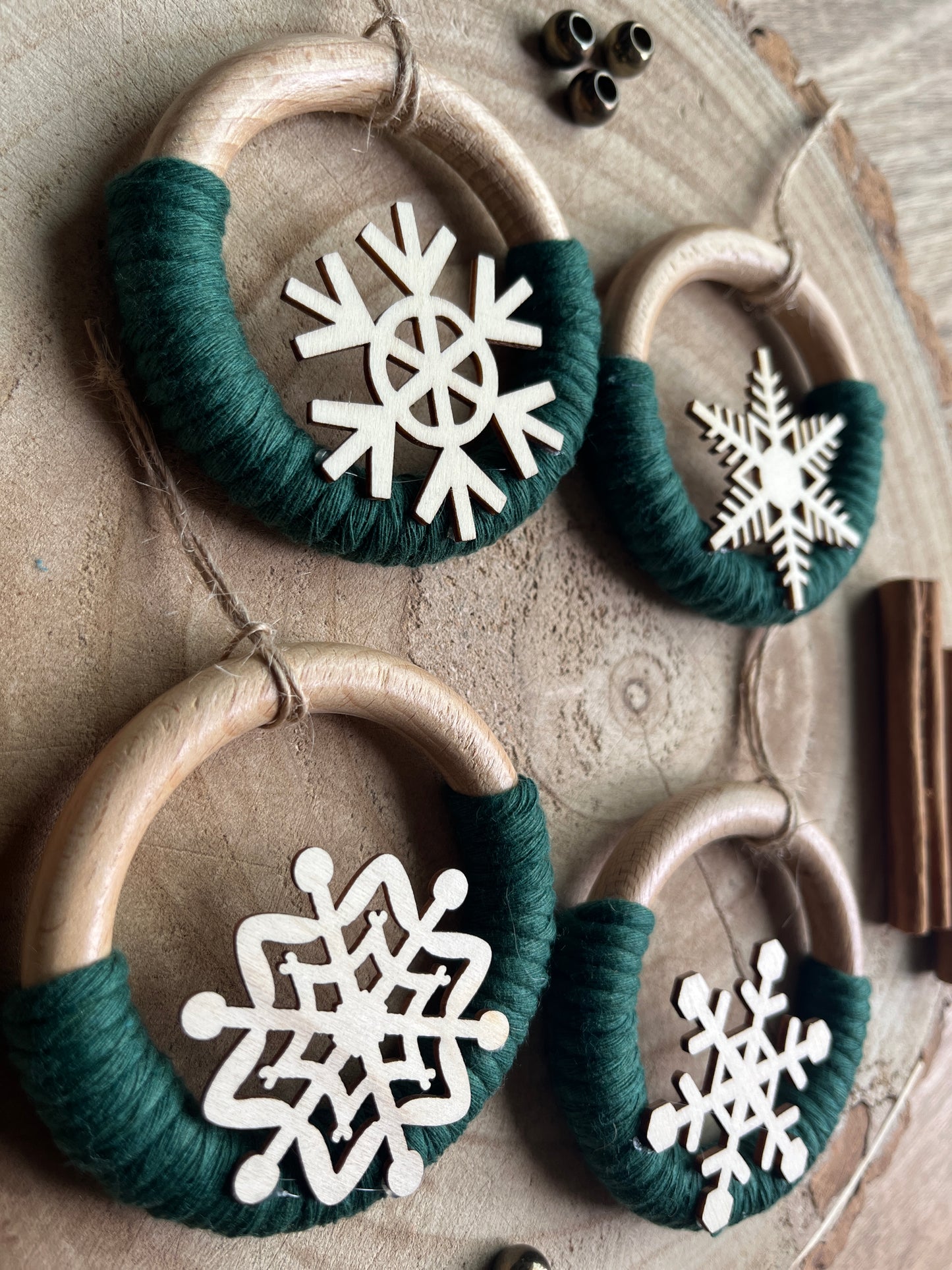 Close up of 4 decorative wooden ornaments, made on wooden rings with green yarn and finished with wooden snowflake designs, displayed on a rustic wooden surface.