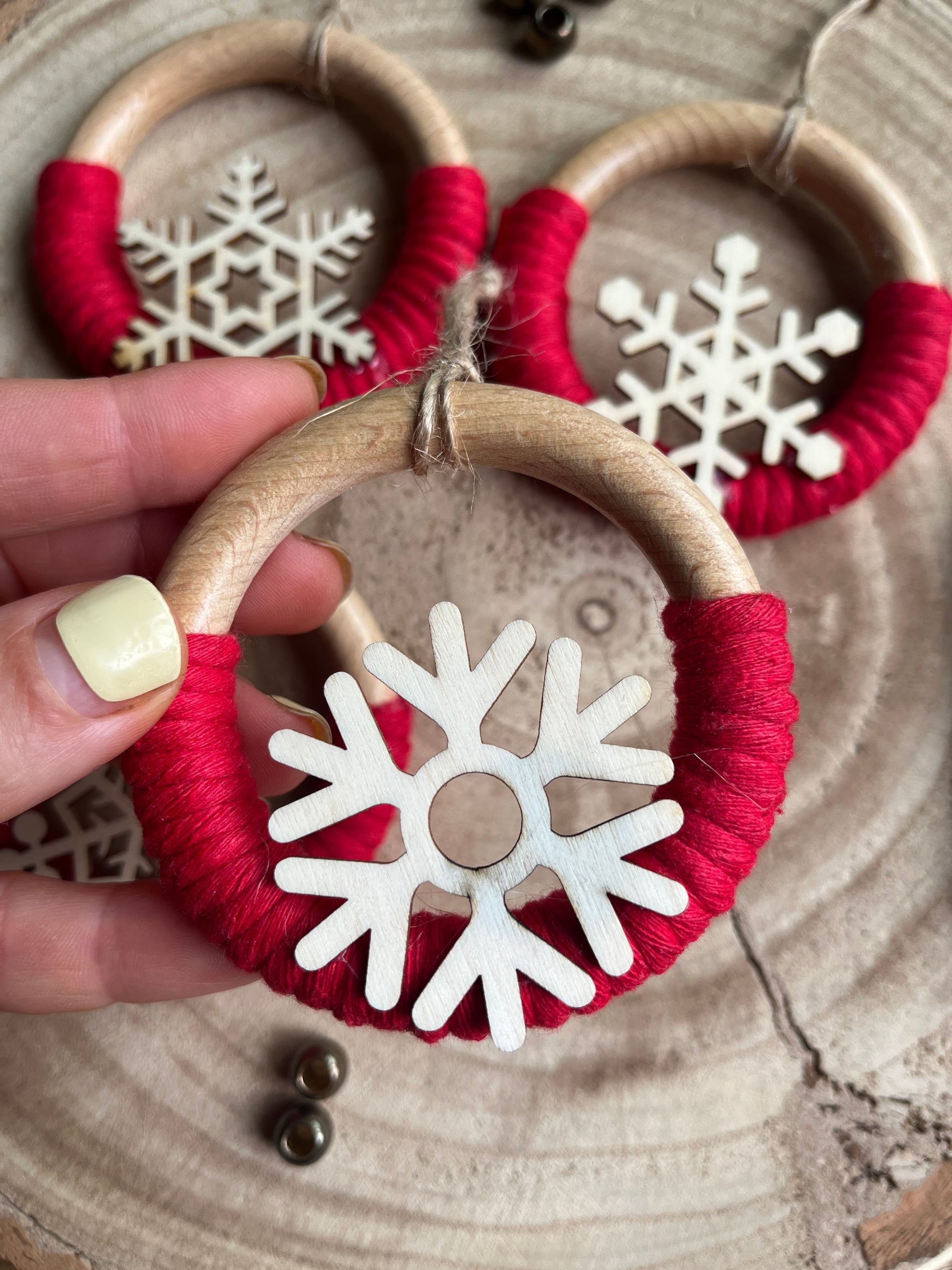 A hand holding a decorative wooden ornament, made on a wooden ring with red yarn and finished with a wooden snowflake design.