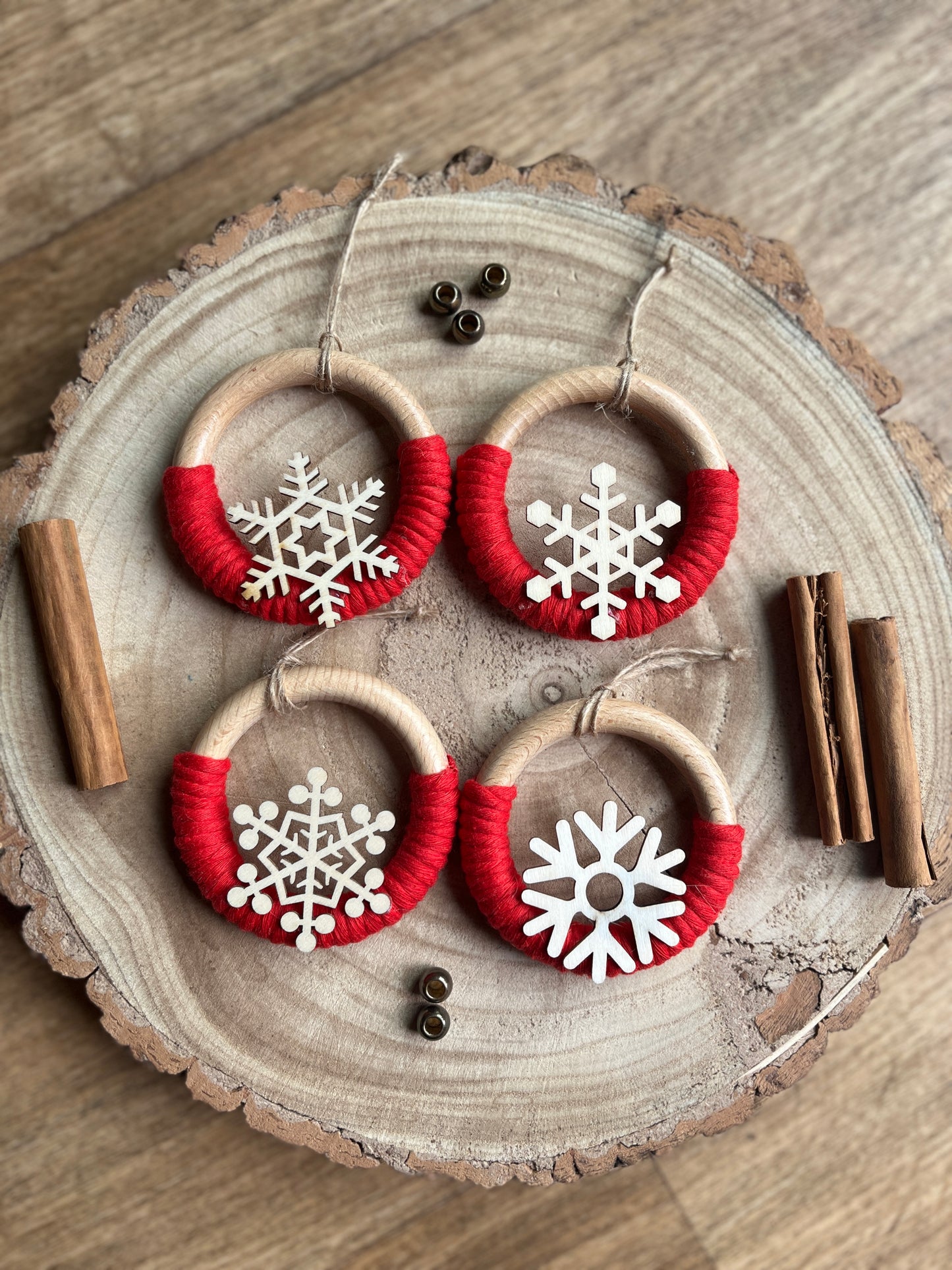 Decorative wooden ornaments, made on wooden rings with red yarn and finished with wooden snowflake designs, displayed on a rustic wooden surface.