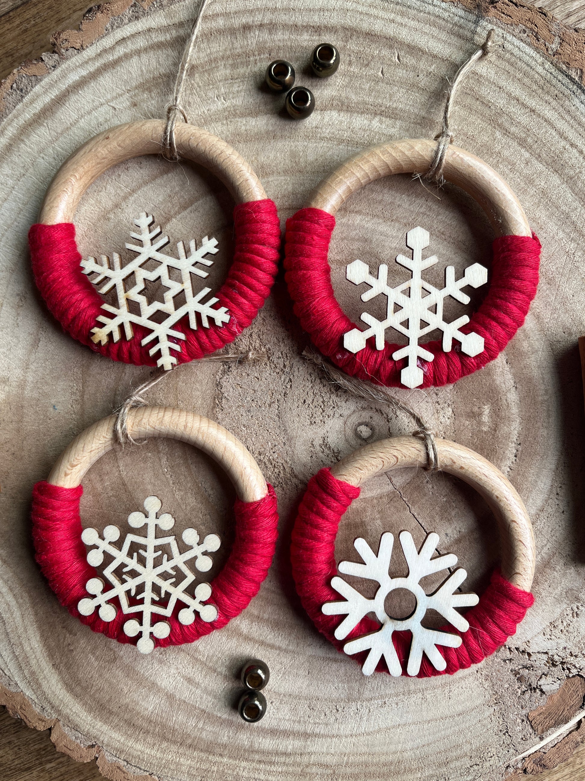 Four decorative wooden ornaments, made on wooden rings with red yarn and finished with wooden snowflake designs, displayed on a rustic wooden surface.