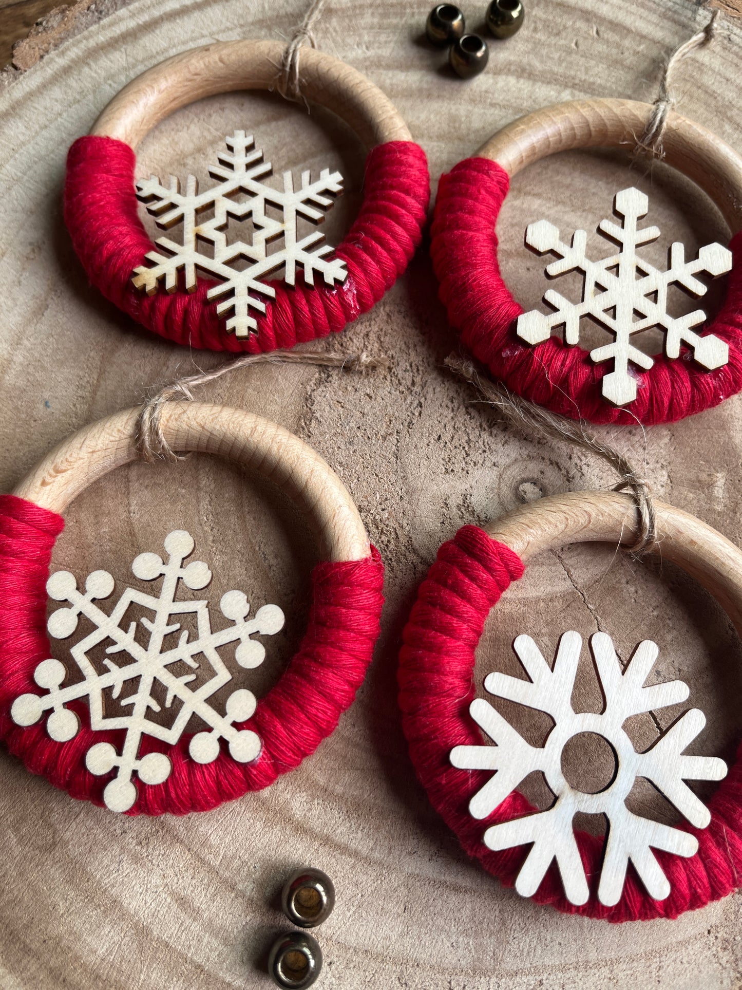Close up of four decorative wooden ornaments, made on wooden rings with red yarn and finished with wooden snowflake designs, displayed on a rustic wooden surface.